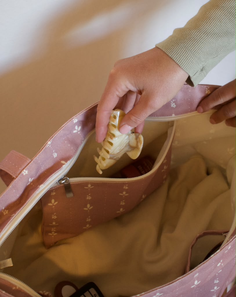 A hair clip placed into the interior zipper pocket of a pink floral Sun Freckled Studio tote bag.
